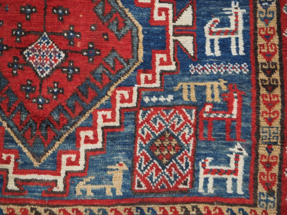 An antique Caucasian Bordjalou Kazak rug featuring a central navy blue field with two large red diamond medallions, zoomorphic animal motifs, and multi-layered geometric borders. View XIII