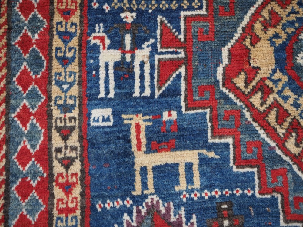 An antique Caucasian Bordjalou Kazak rug featuring a central navy blue field with two large red diamond medallions, zoomorphic animal motifs, and multi-layered geometric borders. View XVII