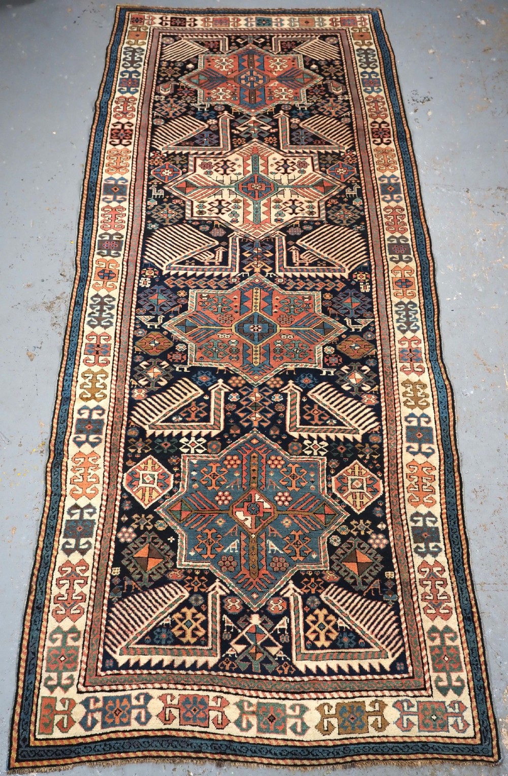An antique Caucasian Akstafa wool rug runner featuring geometric star medallions and stylised peacock motifs on a dark navy field with a decorative border.