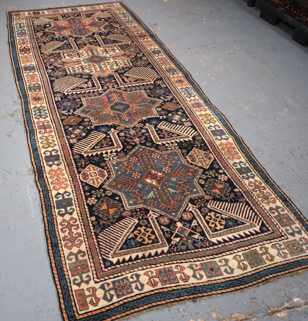 An antique Caucasian Akstafa wool rug runner featuring geometric star medallions and stylised peacock motifs on a dark navy field with a decorative border. View II