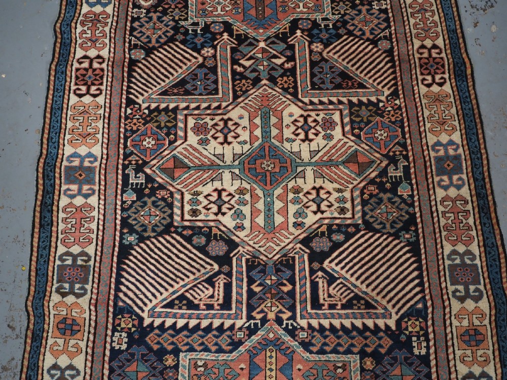 An antique Caucasian Akstafa wool rug runner featuring geometric star medallions and stylised peacock motifs on a dark navy field with a decorative border. View IV