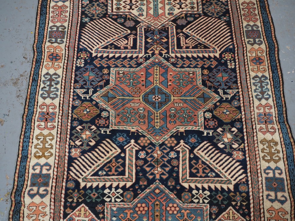 An antique Caucasian Akstafa wool rug runner featuring geometric star medallions and stylised peacock motifs on a dark navy field with a decorative border. View V