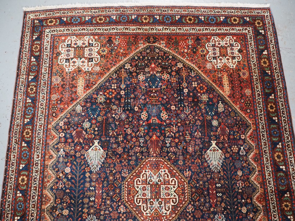 A rectangular hand-knotted antique Abadeh rug featuring a navy blue central field with a diamond medallion and rust red geometric spandrels. View III