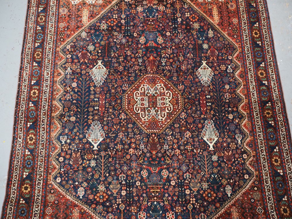 A rectangular hand-knotted antique Abadeh rug featuring a navy blue central field with a diamond medallion and rust red geometric spandrels. View IV