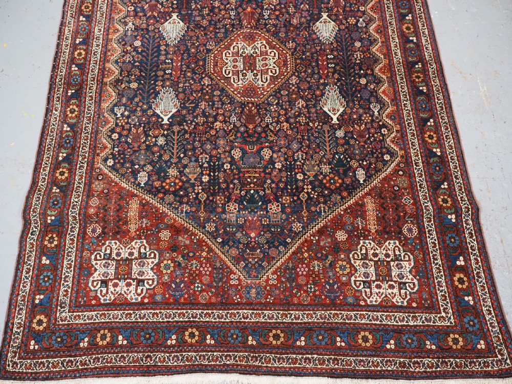 A rectangular hand-knotted antique Abadeh rug featuring a navy blue central field with a diamond medallion and rust red geometric spandrels. View V
