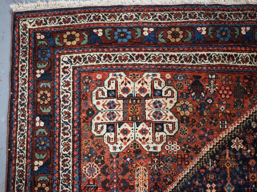A rectangular hand-knotted antique Abadeh rug featuring a navy blue central field with a diamond medallion and rust red geometric spandrels. View VI