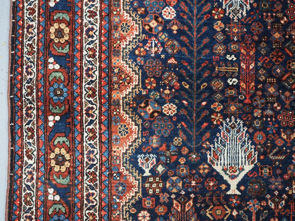 A rectangular hand-knotted antique Abadeh rug featuring a navy blue central field with a diamond medallion and rust red geometric spandrels. View VII