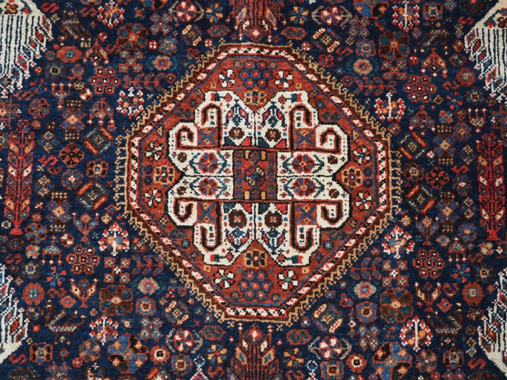 A rectangular hand-knotted antique Abadeh rug featuring a navy blue central field with a diamond medallion and rust red geometric spandrels. View VIII
