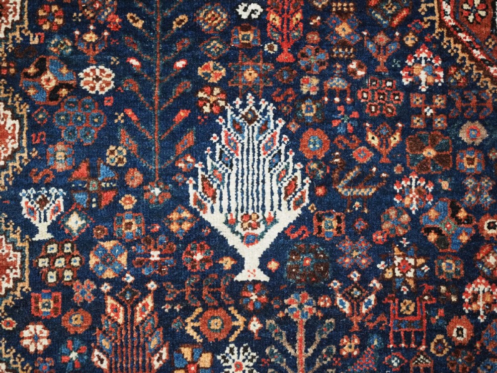 A rectangular hand-knotted antique Abadeh rug featuring a navy blue central field with a diamond medallion and rust red geometric spandrels. View IX