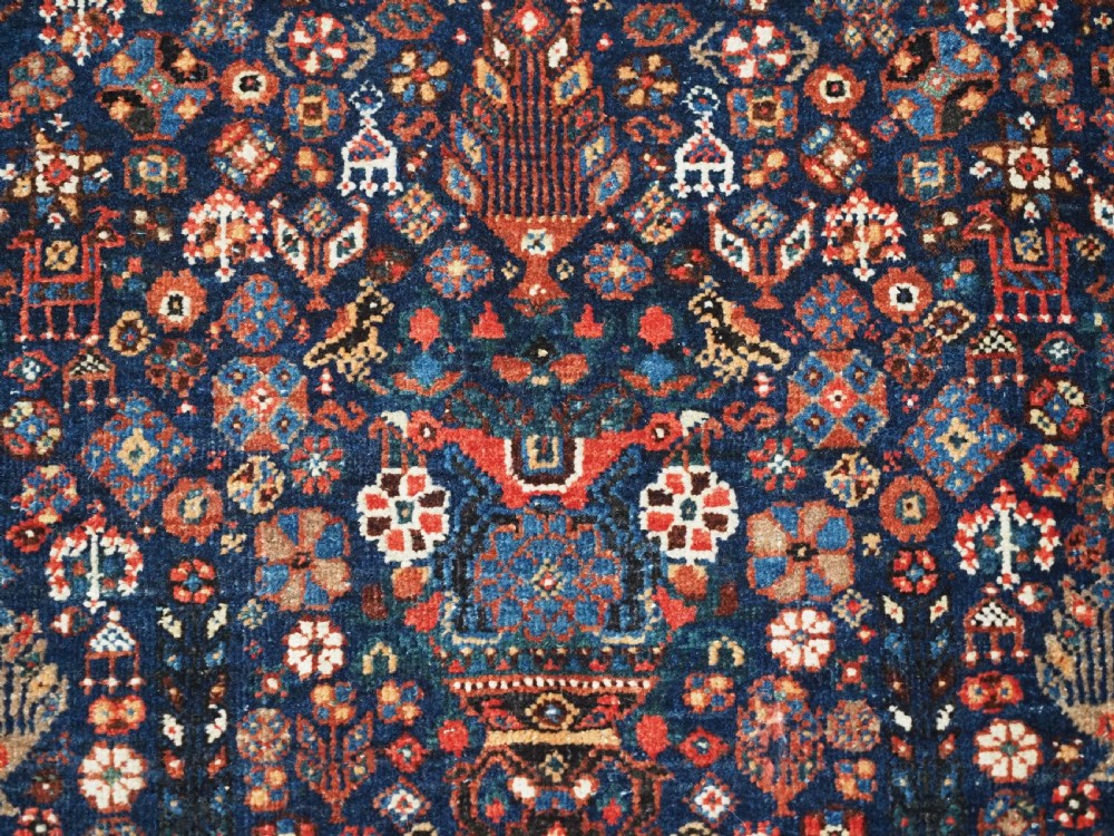 A rectangular hand-knotted antique Abadeh rug featuring a navy blue central field with a diamond medallion and rust red geometric spandrels. View XI