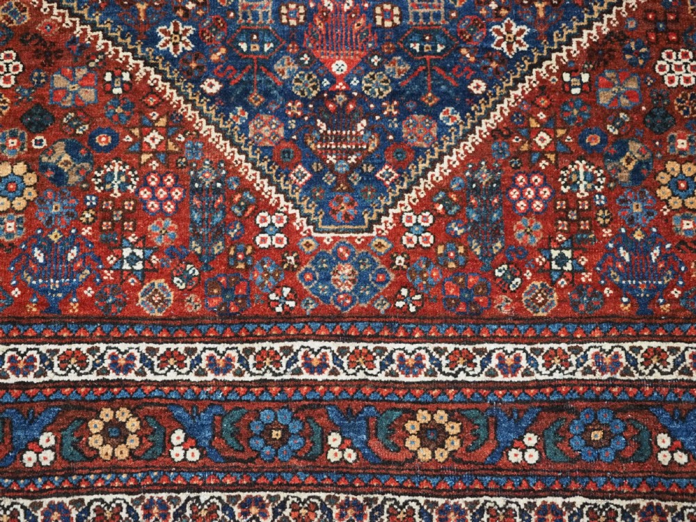 A rectangular hand-knotted antique Abadeh rug featuring a navy blue central field with a diamond medallion and rust red geometric spandrels. View XII