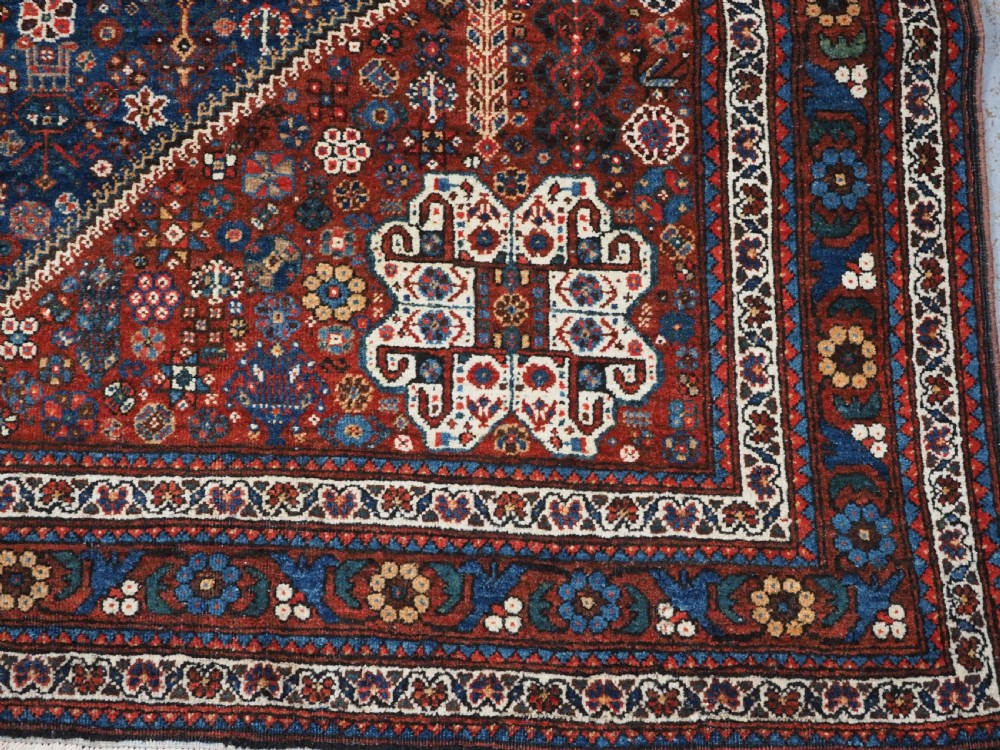 A rectangular hand-knotted antique Abadeh rug featuring a navy blue central field with a diamond medallion and rust red geometric spandrels. View XIII
