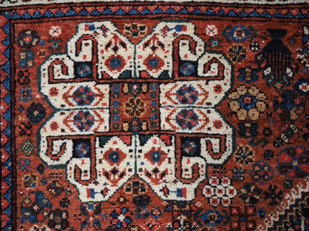 A rectangular hand-knotted antique Abadeh rug featuring a navy blue central field with a diamond medallion and rust red geometric spandrels. View XV
