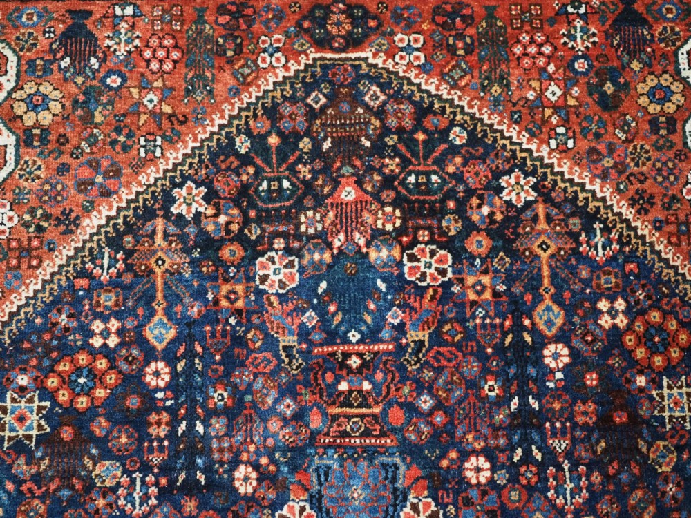 A rectangular hand-knotted antique Abadeh rug featuring a navy blue central field with a diamond medallion and rust red geometric spandrels. View XVI
