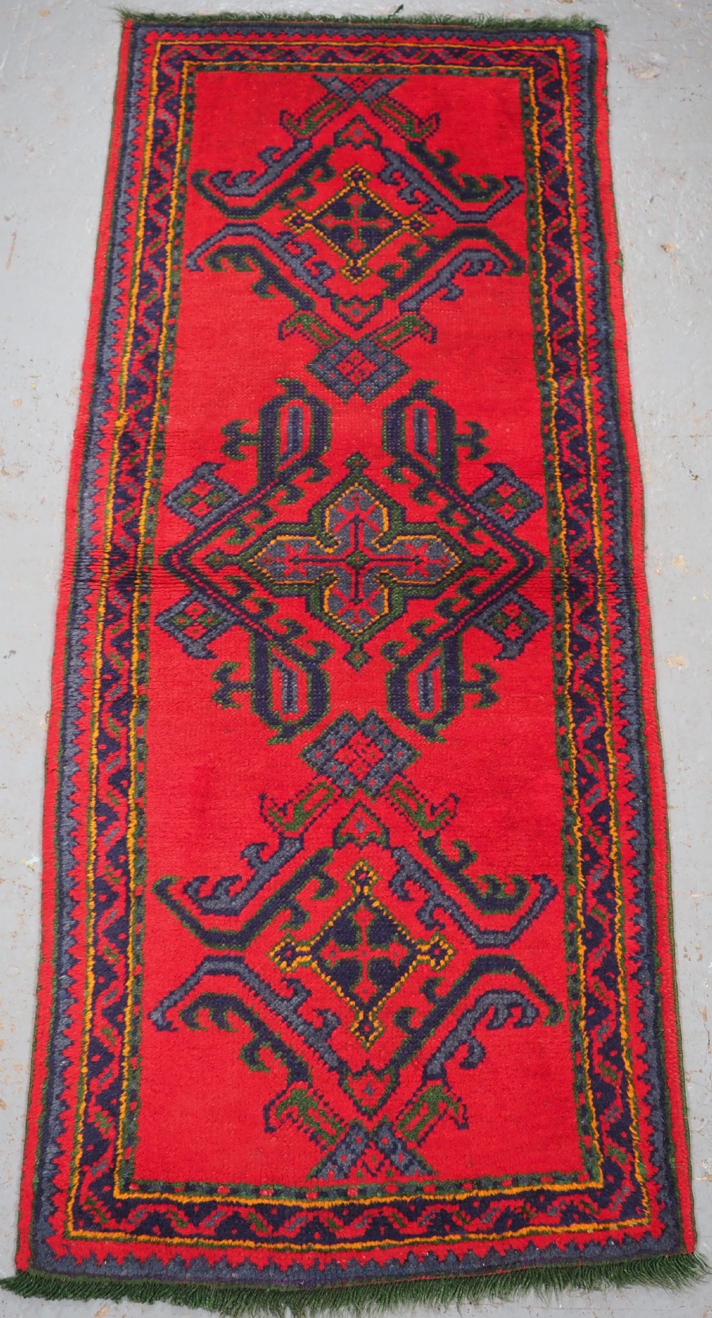 A hand-knotted red wool rug runner featuring geometric central medallions in blue, green, and yellow with a patterned border.