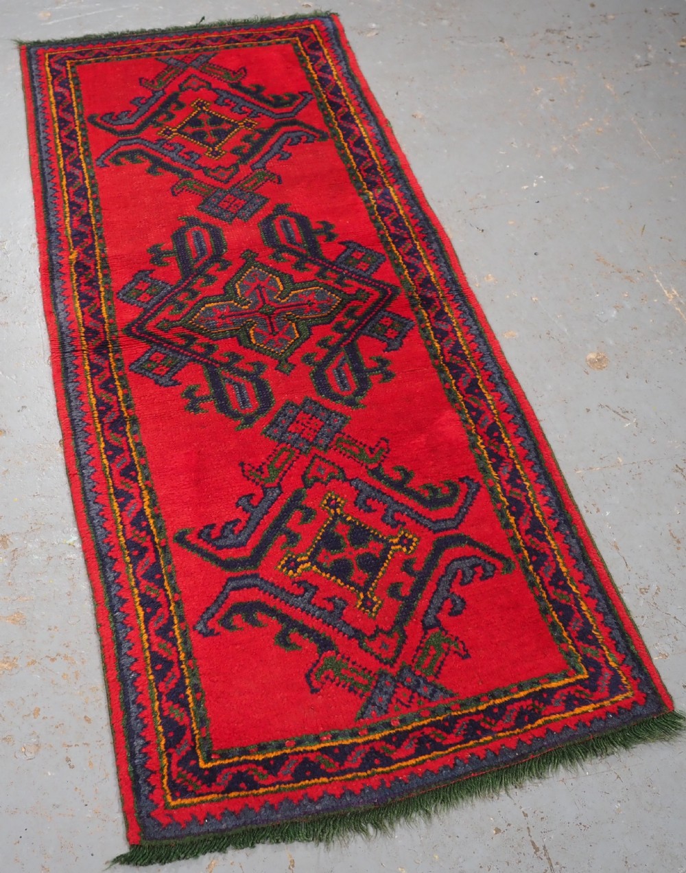 A hand-knotted red wool rug runner featuring geometric central medallions in blue, green, and yellow with a patterned border. View II