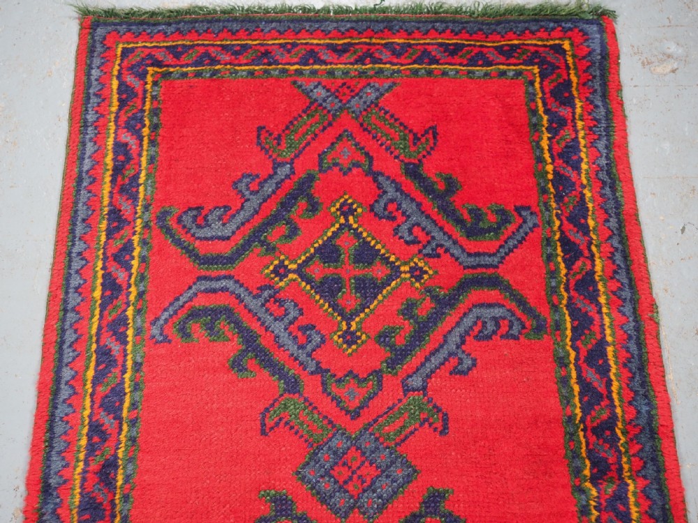 A hand-knotted red wool rug runner featuring geometric central medallions in blue, green, and yellow with a patterned border. View III