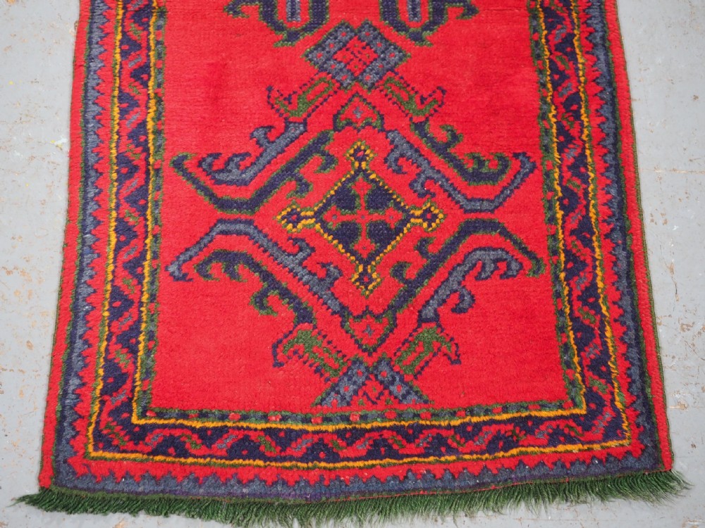 A hand-knotted red wool rug runner featuring geometric central medallions in blue, green, and yellow with a patterned border. View V