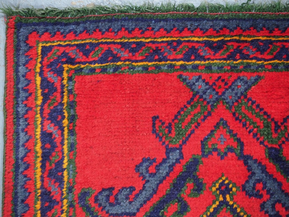 A hand-knotted red wool rug runner featuring geometric central medallions in blue, green, and yellow with a patterned border. View VI