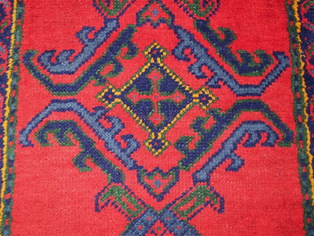 A hand-knotted red wool rug runner featuring geometric central medallions in blue, green, and yellow with a patterned border. View VIII