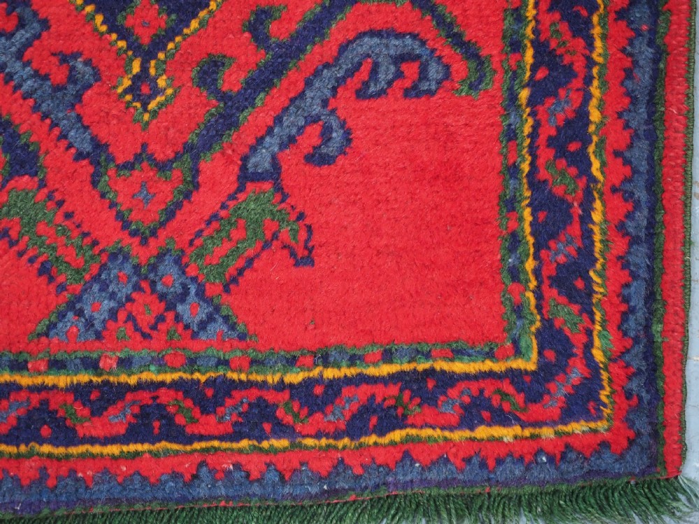 A hand-knotted red wool rug runner featuring geometric central medallions in blue, green, and yellow with a patterned border. View XI