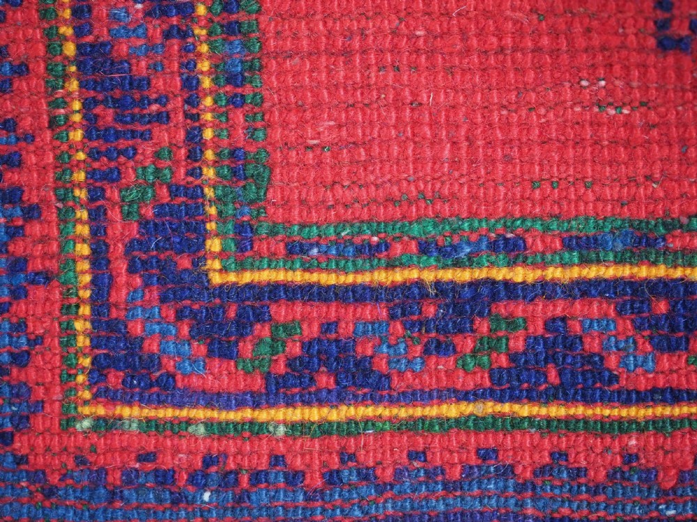 A hand-knotted red wool rug runner featuring geometric central medallions in blue, green, and yellow with a patterned border. View XII