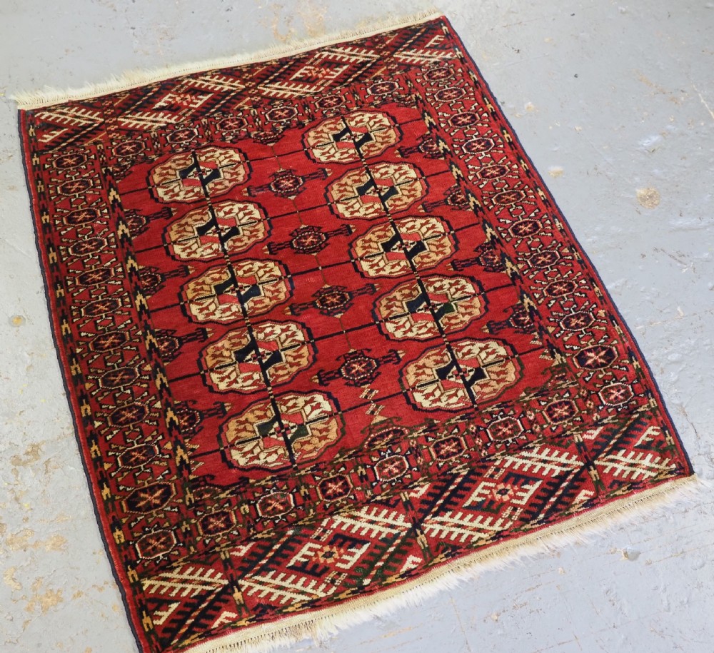 A small rectangular Tekke Turkmen hand-knotted wool rug featuring two vertical columns of geometric octagonal guls on a deep red ground with patterned borders and fringed edges. View II