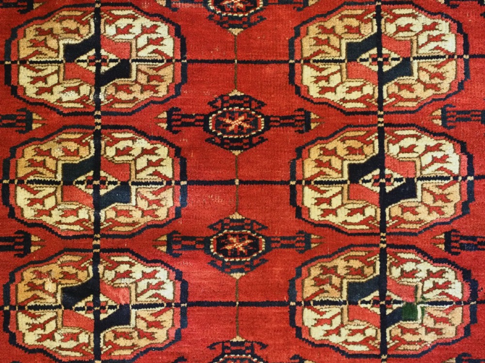 A small rectangular Tekke Turkmen hand-knotted wool rug featuring two vertical columns of geometric octagonal guls on a deep red ground with patterned borders and fringed edges. View VII