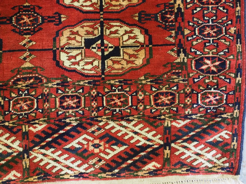 A small rectangular Tekke Turkmen hand-knotted wool rug featuring two vertical columns of geometric octagonal guls on a deep red ground with patterned borders and fringed edges. View VIII