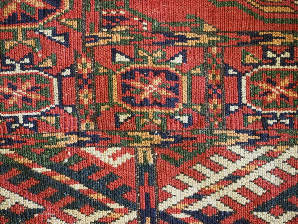 A small rectangular Tekke Turkmen hand-knotted wool rug featuring two vertical columns of geometric octagonal guls on a deep red ground with patterned borders and fringed edges. View IX