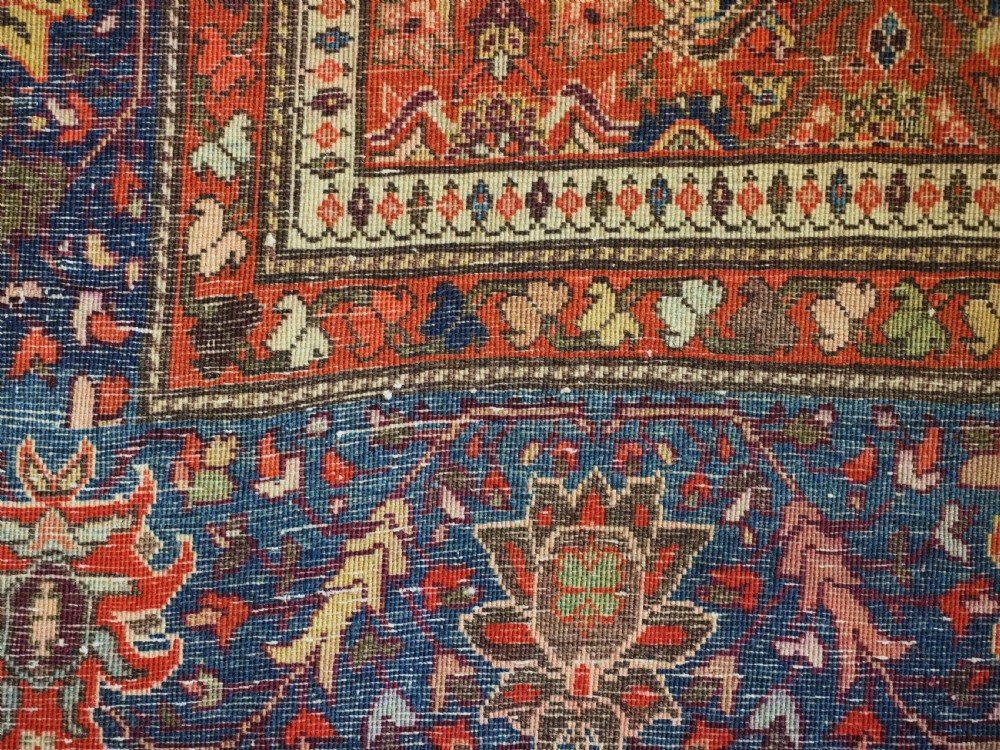 An antique Persian Sarouk rug featuring a repeating central boteh pattern framed by detailed floral borders in shades of terracotta red, cream, and navy blue. View II
