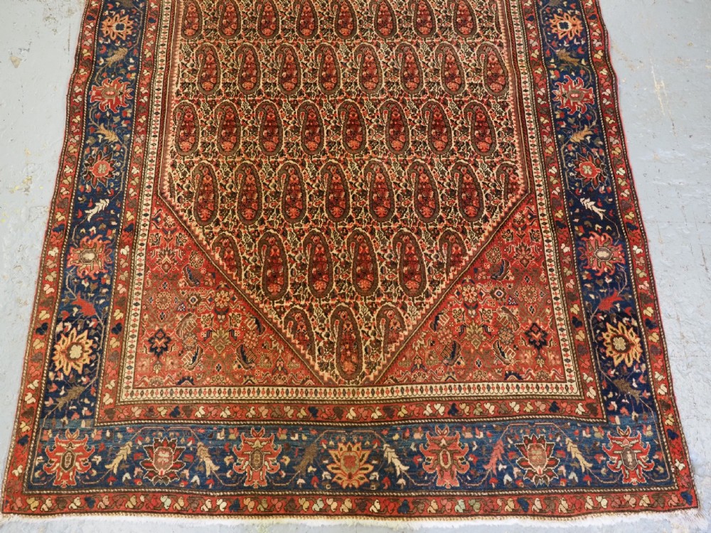 An antique Persian Sarouk rug featuring a repeating central boteh pattern framed by detailed floral borders in shades of terracotta red, cream, and navy blue. View VI