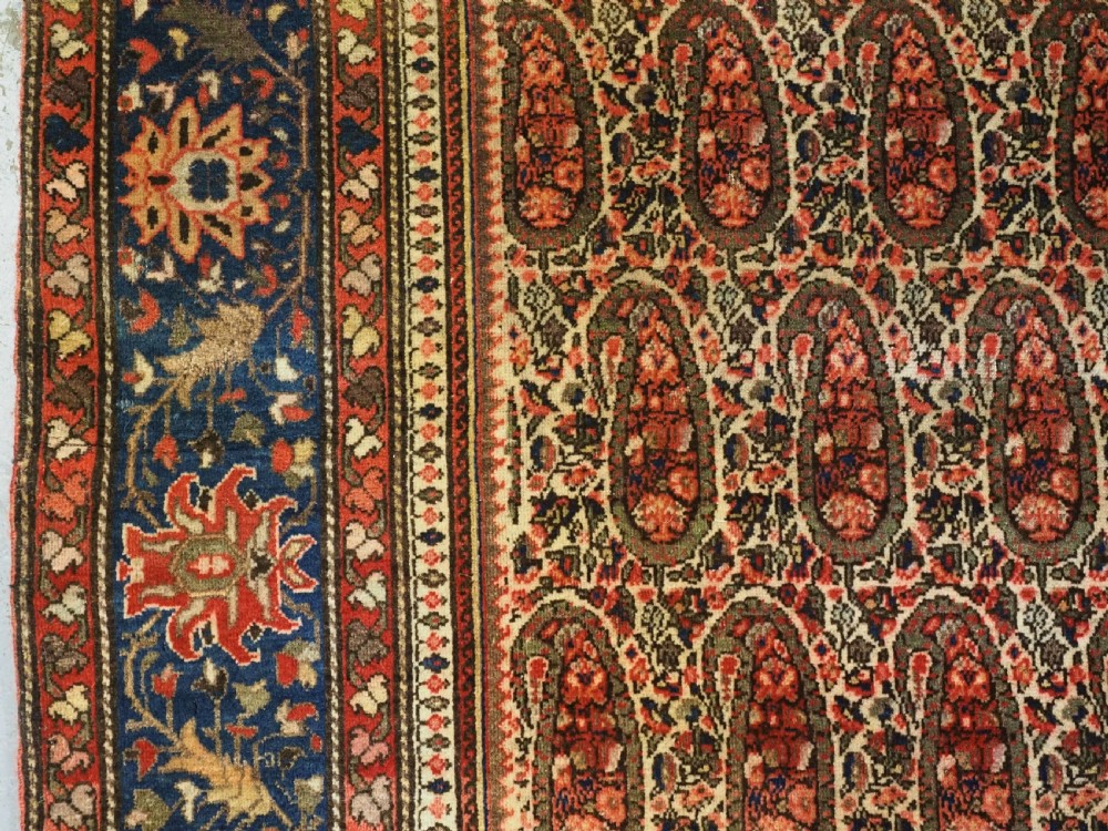 An antique Persian Sarouk rug featuring a repeating central boteh pattern framed by detailed floral borders in shades of terracotta red, cream, and navy blue. View VIII