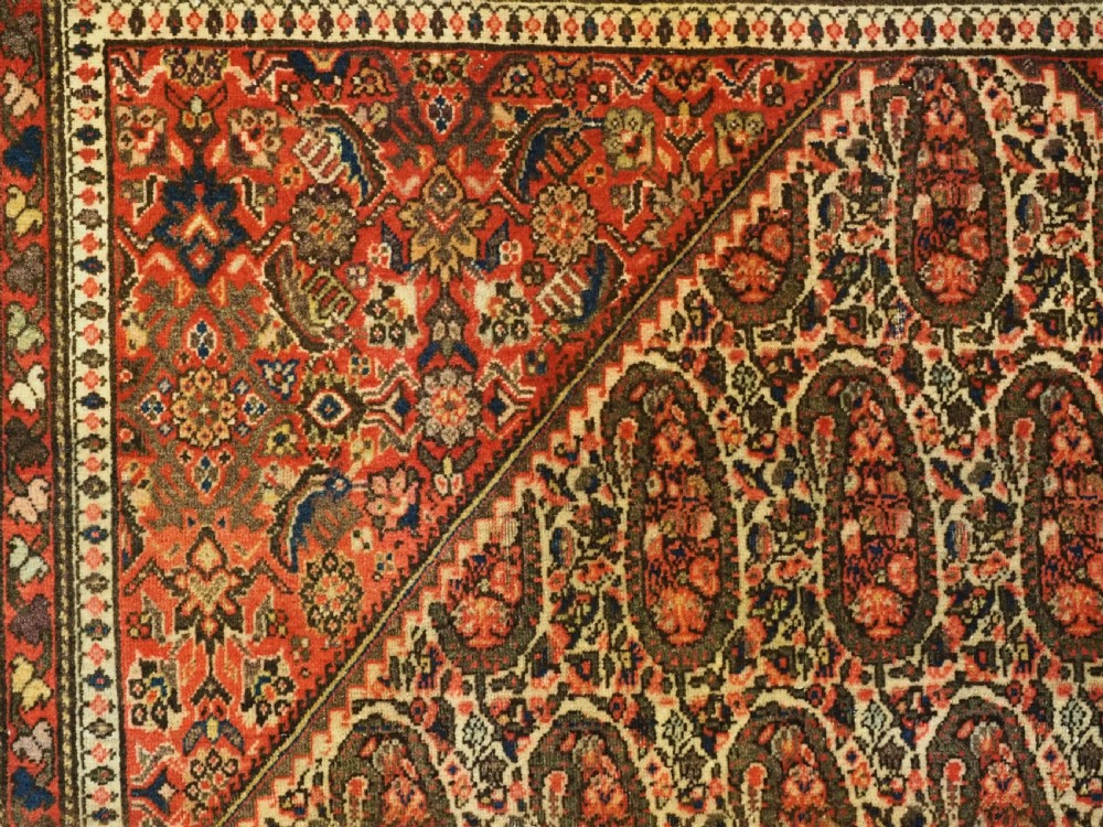 An antique Persian Sarouk rug featuring a repeating central boteh pattern framed by detailed floral borders in shades of terracotta red, cream, and navy blue. View IX