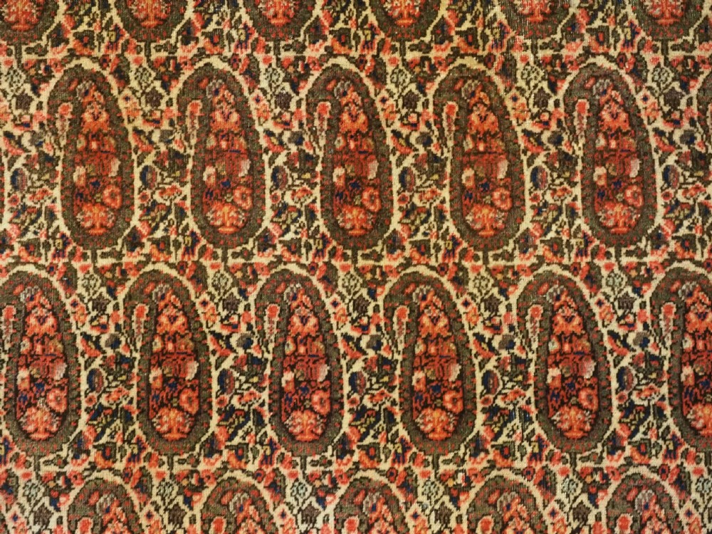 An antique Persian Sarouk rug featuring a repeating central boteh pattern framed by detailed floral borders in shades of terracotta red, cream, and navy blue. View X