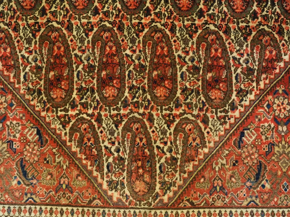 An antique Persian Sarouk rug featuring a repeating central boteh pattern framed by detailed floral borders in shades of terracotta red, cream, and navy blue. View XI