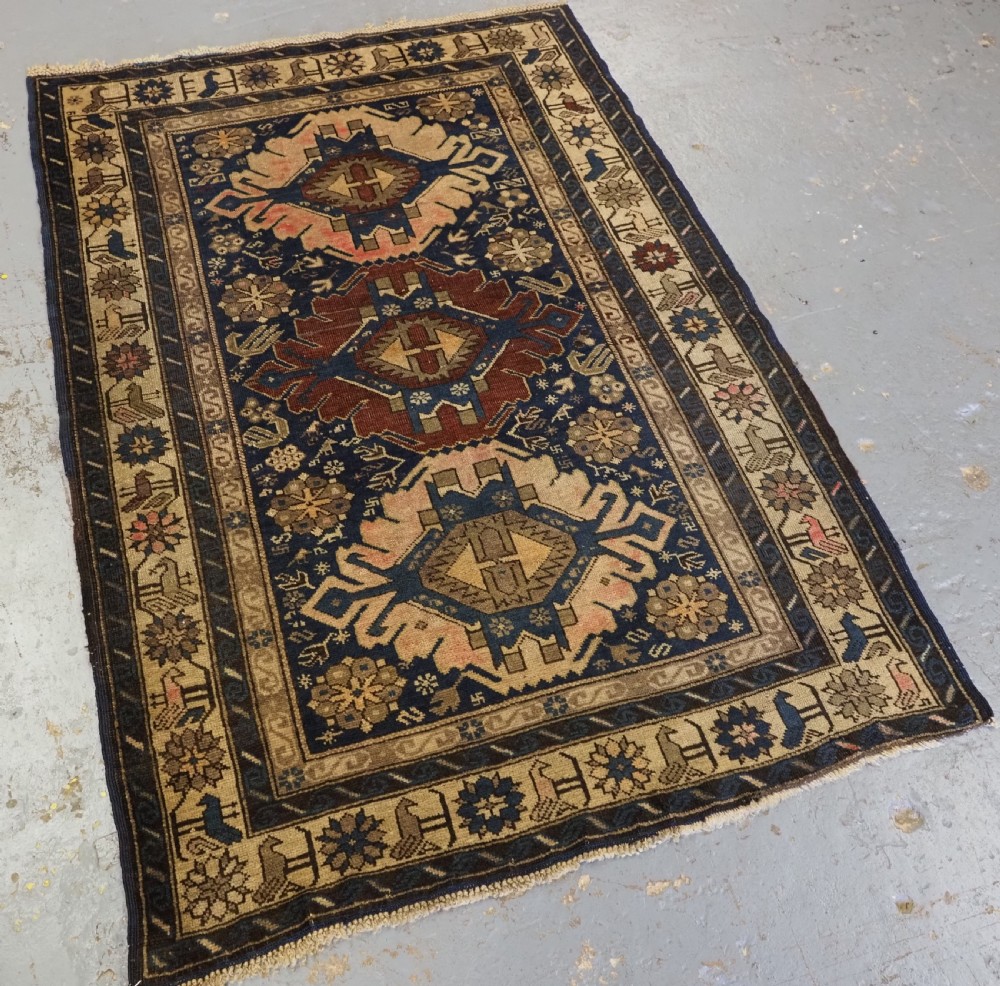 An antique hand-knotted Caucasian rug featuring three central geometric medallions on a navy blue field with a beige border adorned with stylized bird motifs. View II
