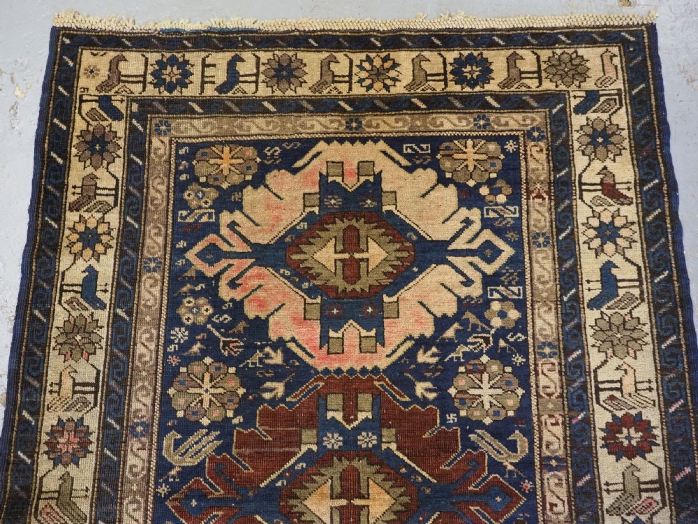 An antique hand-knotted Caucasian rug featuring three central geometric medallions on a navy blue field with a beige border adorned with stylized bird motifs. View III