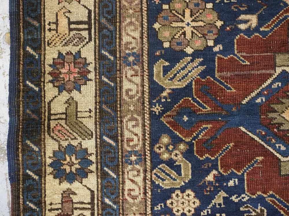 An antique hand-knotted Caucasian rug featuring three central geometric medallions on a navy blue field with a beige border adorned with stylized bird motifs. View VII