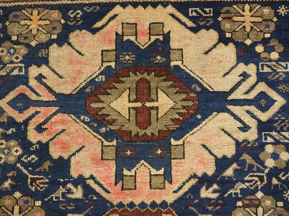 An antique hand-knotted Caucasian rug featuring three central geometric medallions on a navy blue field with a beige border adorned with stylized bird motifs. View VIII