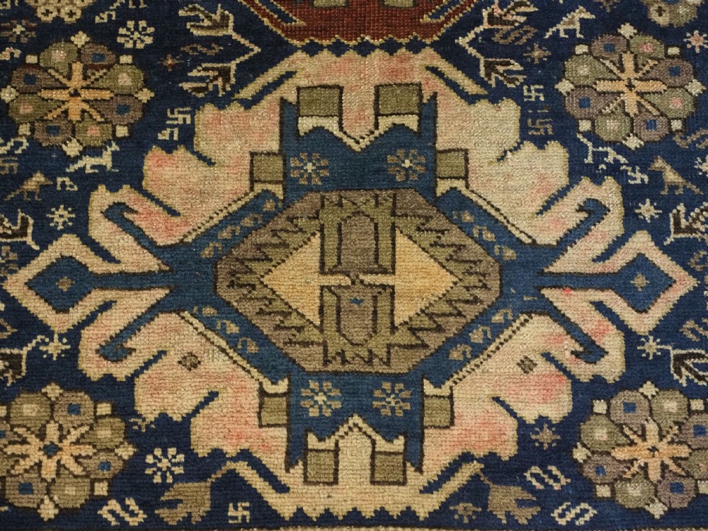 An antique hand-knotted Caucasian rug featuring three central geometric medallions on a navy blue field with a beige border adorned with stylized bird motifs. View X