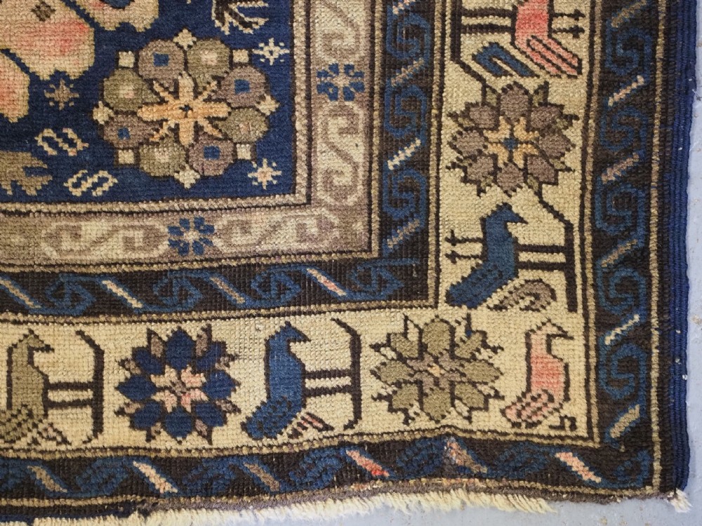 An antique hand-knotted Caucasian rug featuring three central geometric medallions on a navy blue field with a beige border adorned with stylized bird motifs. View XI