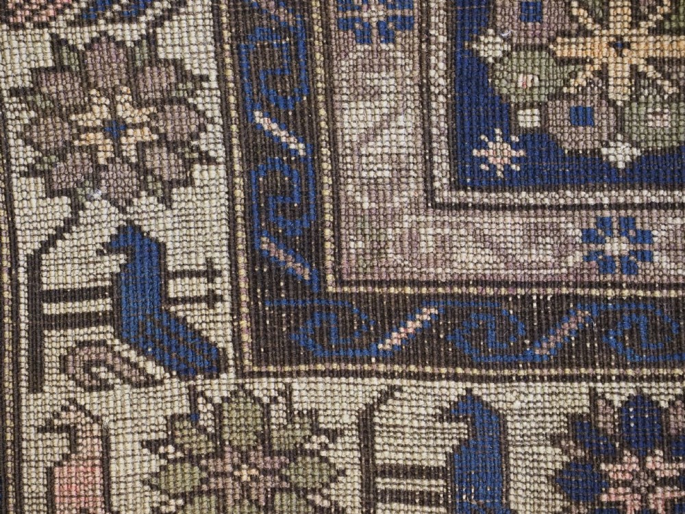 An antique hand-knotted Caucasian rug featuring three central geometric medallions on a navy blue field with a beige border adorned with stylized bird motifs. View XII