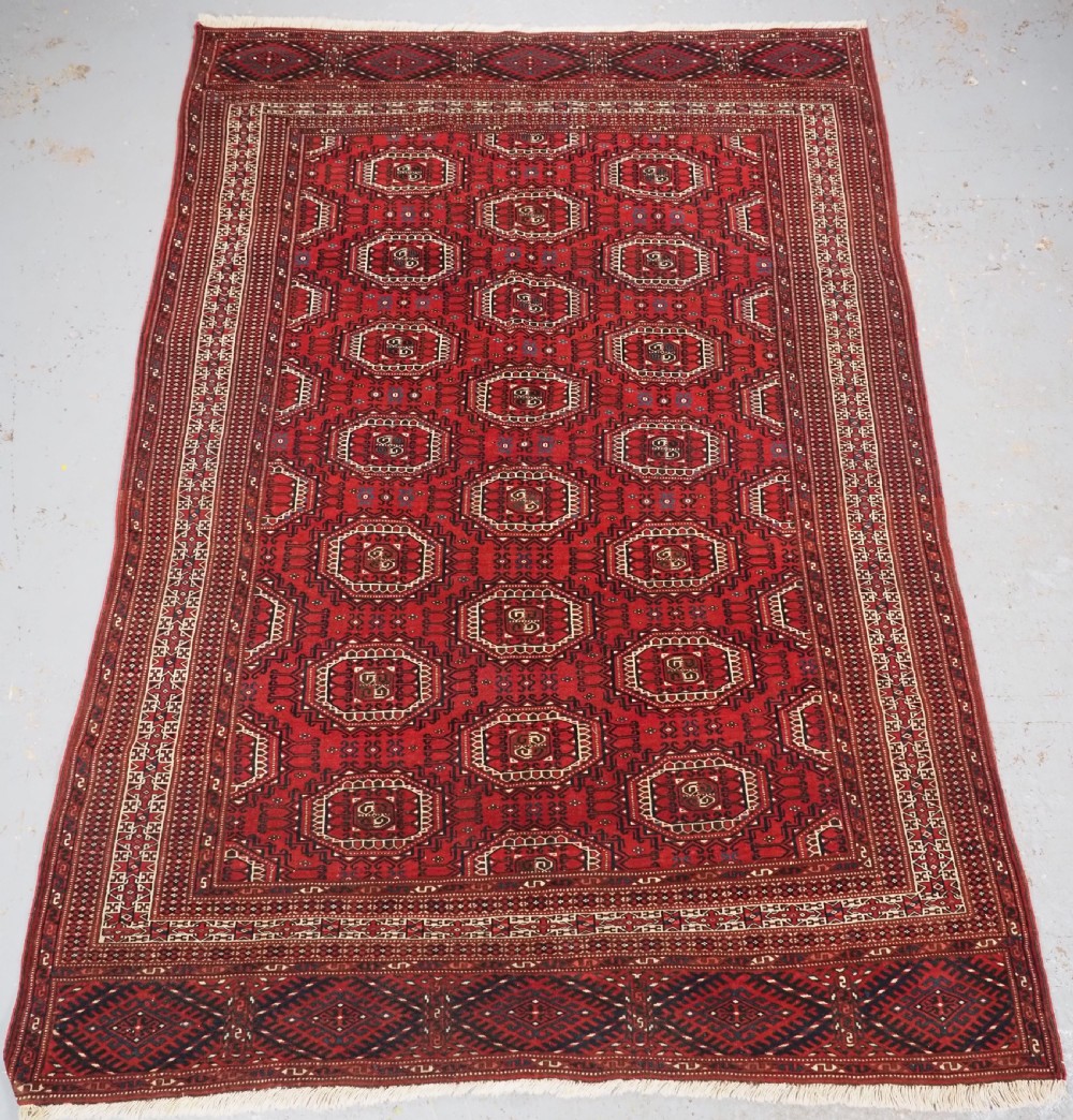 An antique deep red Yomut Turkmen wool rug featuring repeating octagonal guls and intricate geometric borders.