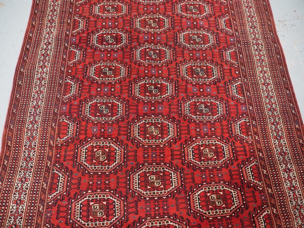 An antique deep red Yomut Turkmen wool rug featuring repeating octagonal guls and intricate geometric borders. View IV