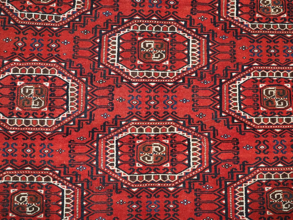 An antique deep red Yomut Turkmen wool rug featuring repeating octagonal guls and intricate geometric borders. View X