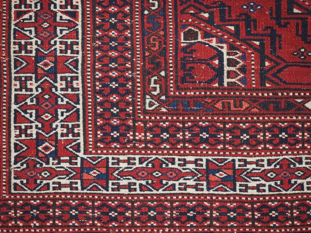 An antique deep red Yomut Turkmen wool rug featuring repeating octagonal guls and intricate geometric borders. View XII