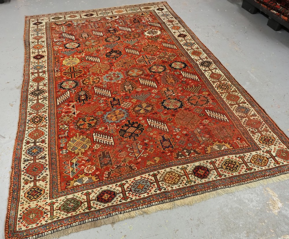 An antique South Persian Shekarlu Qashqai wool rug featuring a red field with dense geometric tribal motifs surrounded by an ivory patterned border. View II