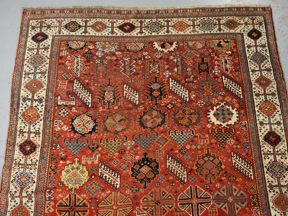 An antique South Persian Shekarlu Qashqai wool rug featuring a red field with dense geometric tribal motifs surrounded by an ivory patterned border. View III