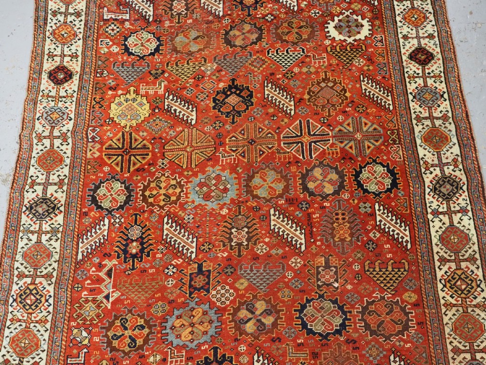 An antique South Persian Shekarlu Qashqai wool rug featuring a red field with dense geometric tribal motifs surrounded by an ivory patterned border. View IV